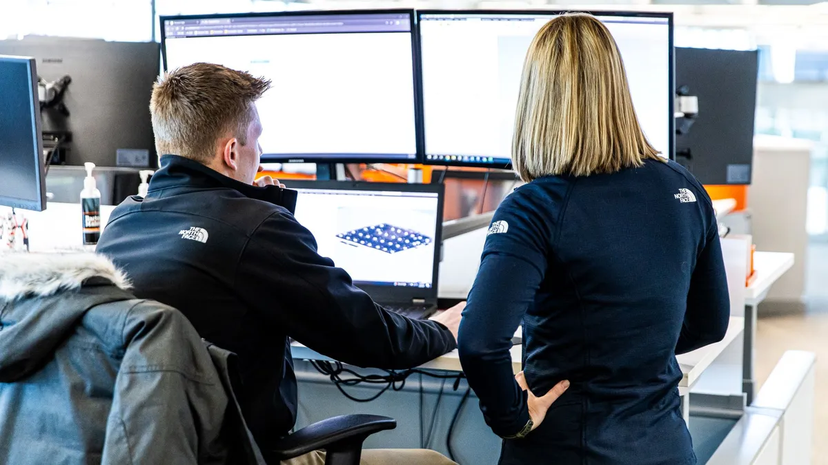 a man and woman look at a computer monitor set up on a construction site