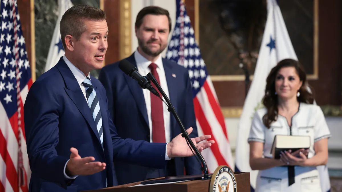 Two men in suits and a woman in the background.