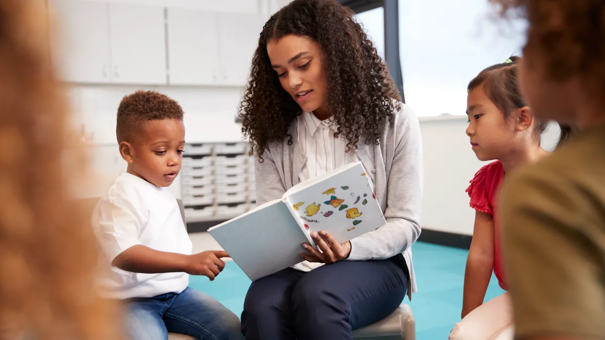 A female teacher of color reads to young students in a classroom.