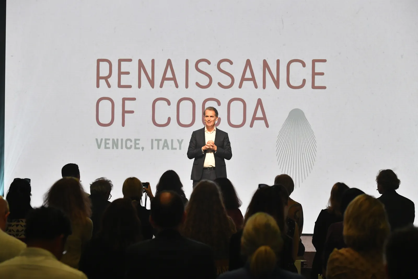 Barry Callebaut CEO Peter Boone speaks on a stage with a white backdrop that says Renaissance of Cocoa behind him.