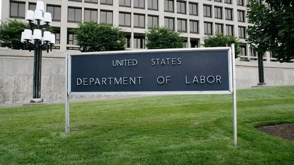 A dark Department of Labor sign in front of a white building with windows.