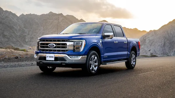 A blue 2021 Ford F-150 pickup on a road with mountains in the background.