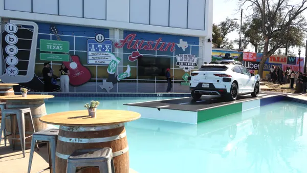 A white car on a platform in front of a building with signs reading "Austin," "Texas" and "Uber."
