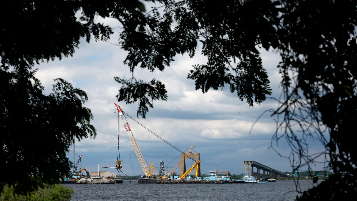 Cranes on barges pick debris out of the water, with a broken bridge in the background.