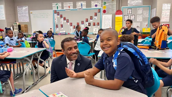 Superintendent Tony Watlington crouches at a desk to talk to an elementary student during a school visit in August 2024.