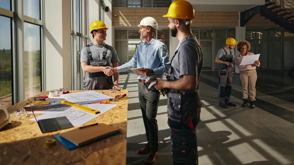A group of people in construction safety gear shake hands on a jobsite.