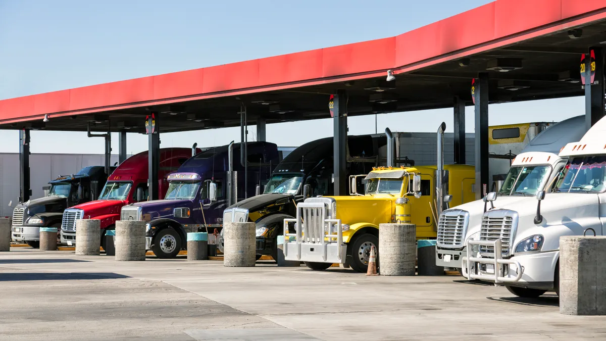 A row of seven trucks filling up at truck stop on a sunny day in California.