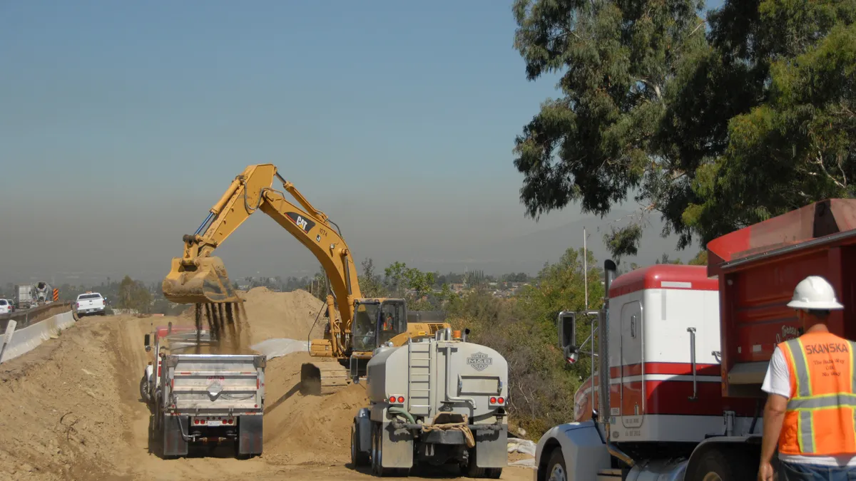 Construction trucks and machinery work along a dirt road.