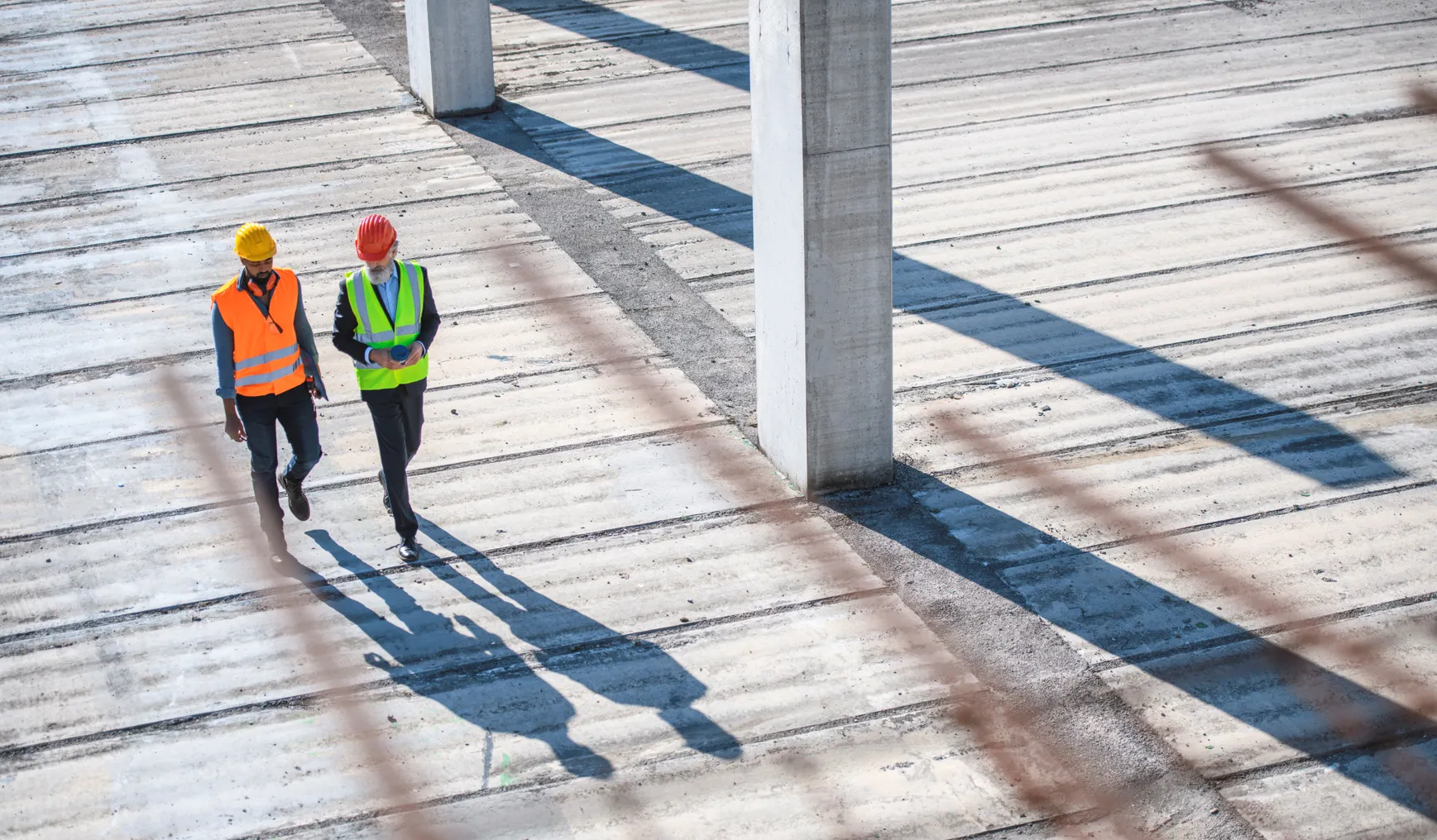 An aerial view of two people on a construction site, walking together.