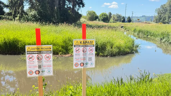 Two signs posted in a surface ditch warn people to stay away from the waterways.