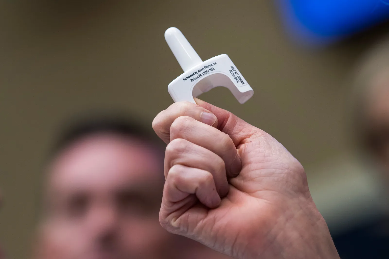 A hand holds a nasal spray device.