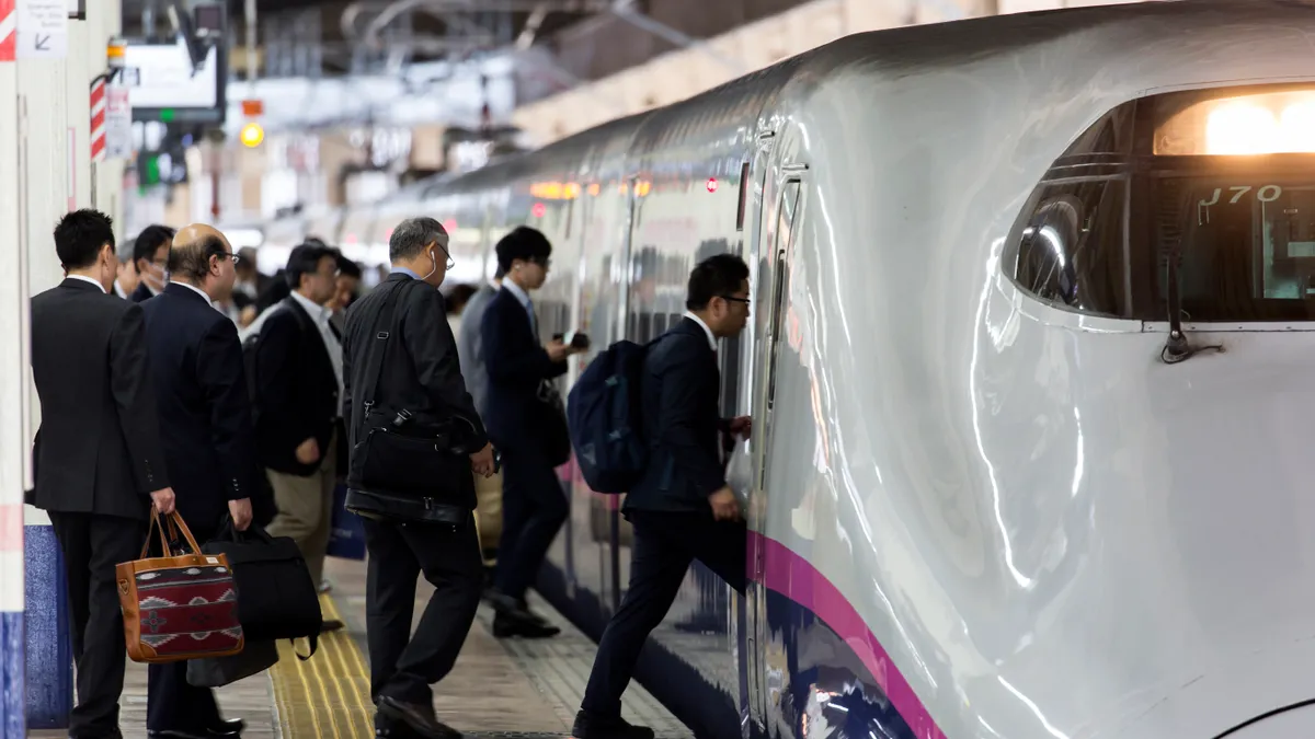 Many men in suites board a high-speed train in Japan.