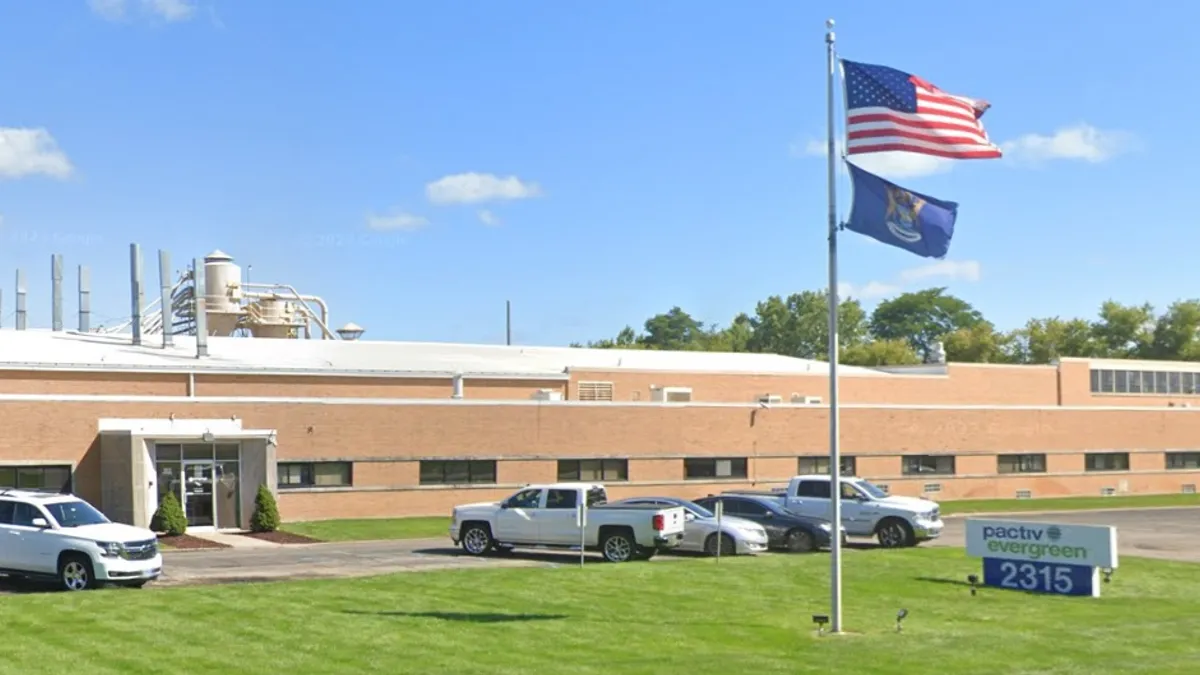 The exterior of an industrial facility with an American flag on the front lawn next to a sign that says Pactiv Evergreen.