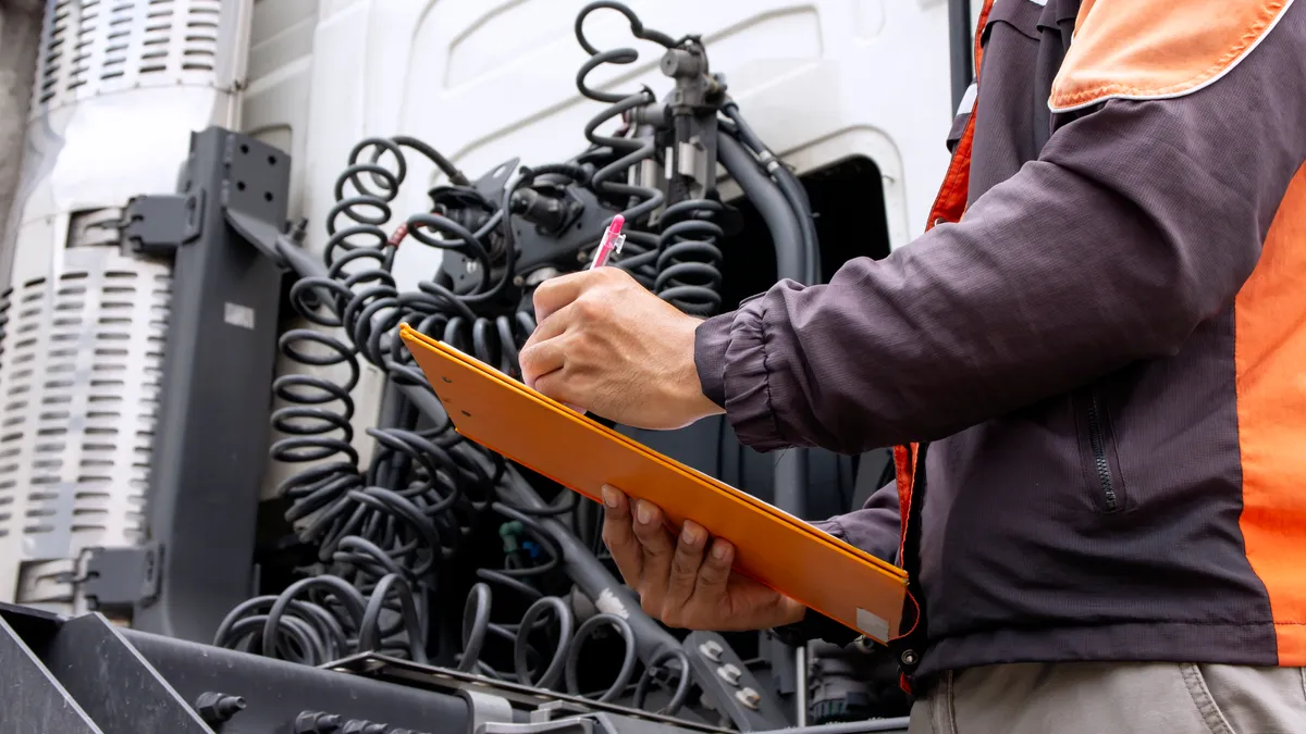 A truck driver holds an orange clipboard while inspecting a vehicle.