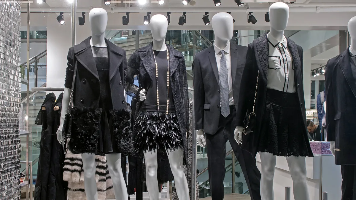 A DKNY storefront mannequin display. Four mannequins wear black, white and grey apparel, including blazers and skirts.