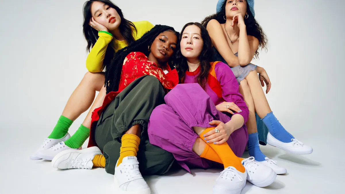 A group of models in colorful attire show off Keds sneakers against a white backdrop.