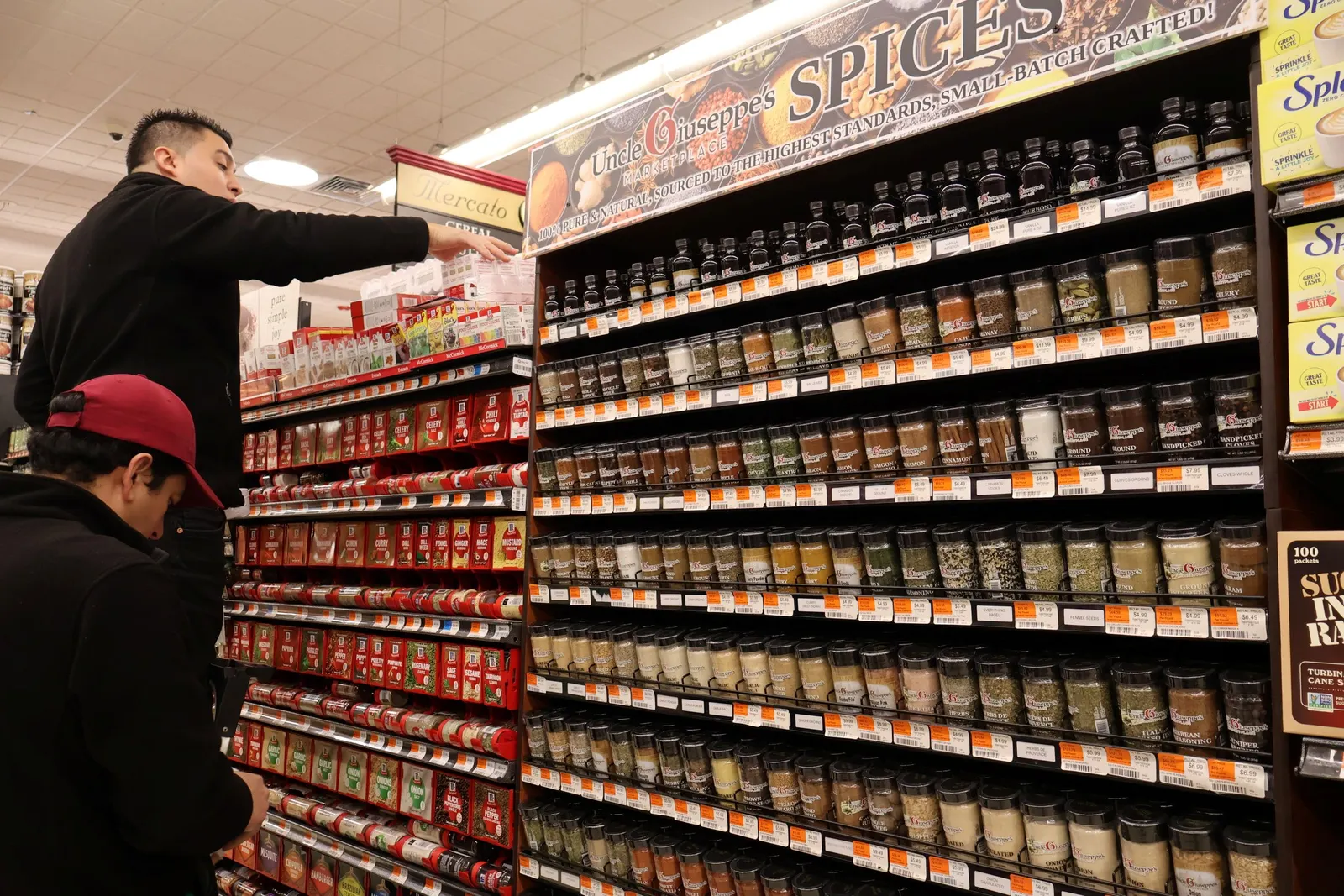 Two grocery store workers stocking spices on the shelves