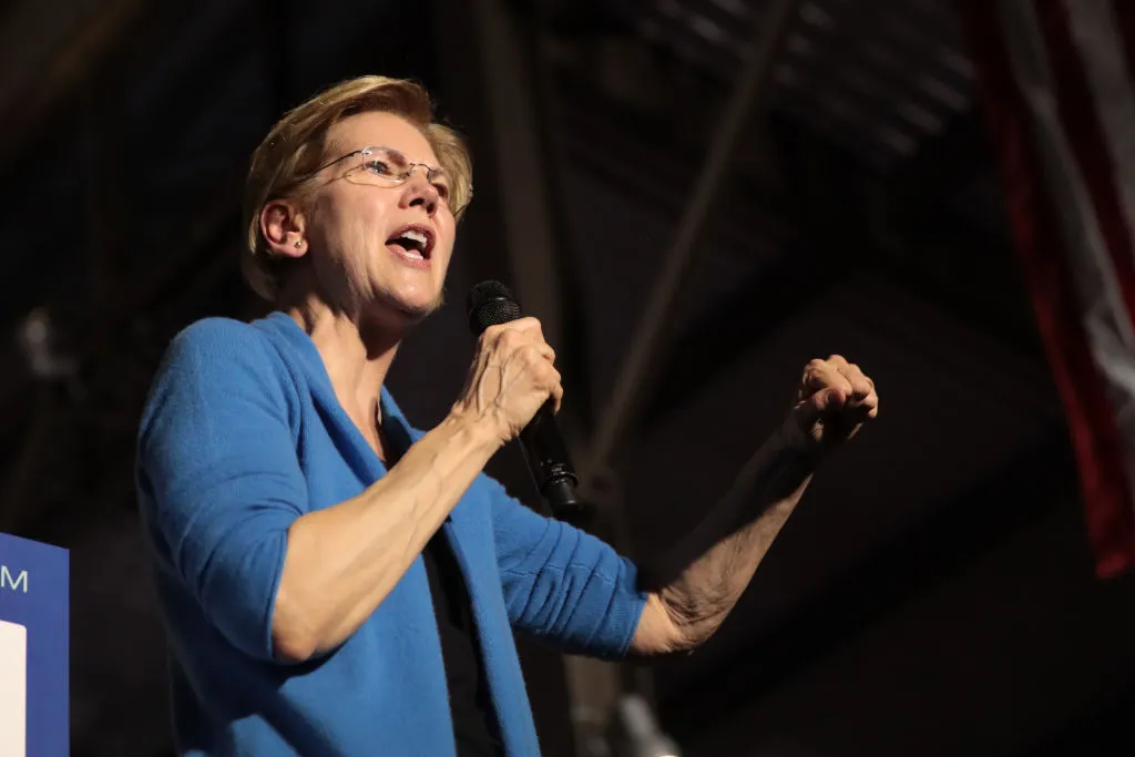 Democratic Sen. Elizabeth Warren stands on stage with one hand holding microphone and the other raised.