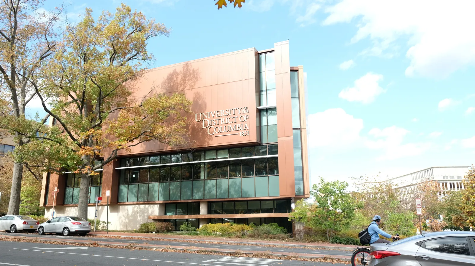 UDC building seen from street as vehicle and bicyclist pass by.