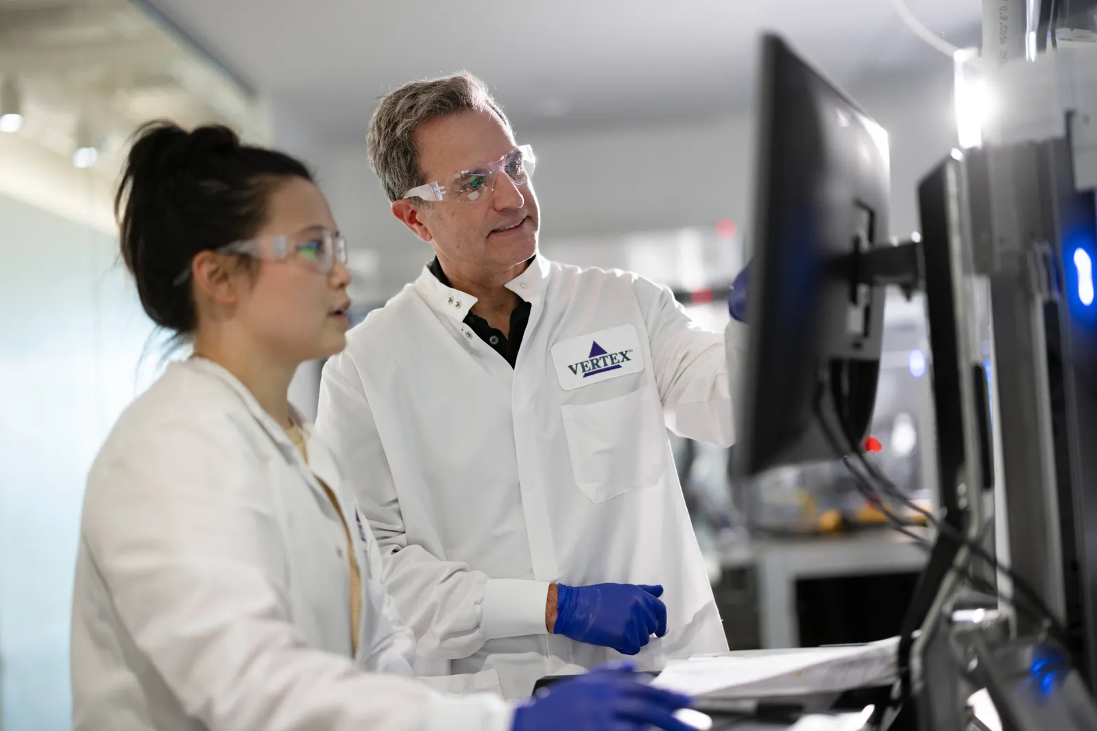 Two people in white coats look at a computer monitor in a research laboratory.