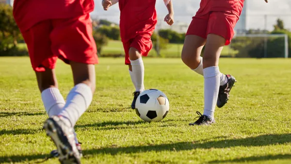 Three students wearing red uniforms pass a soccer ball on an outdoor field.