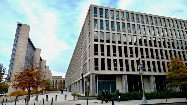 The outside of the U.S. Department of Education in Washington, D.C. is shown on a close day. People are walking on the sidewalk in front of the building.