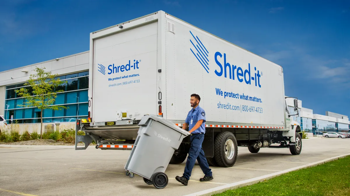 A driver stands next to a shredding truck.