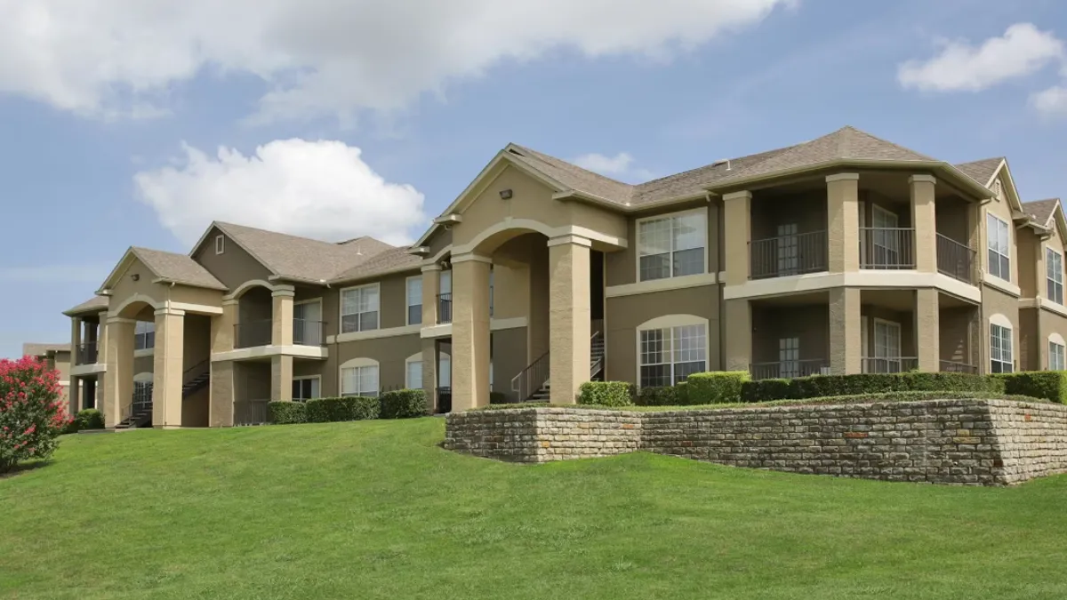 Two-story brown apartment community with grass in the foreground.