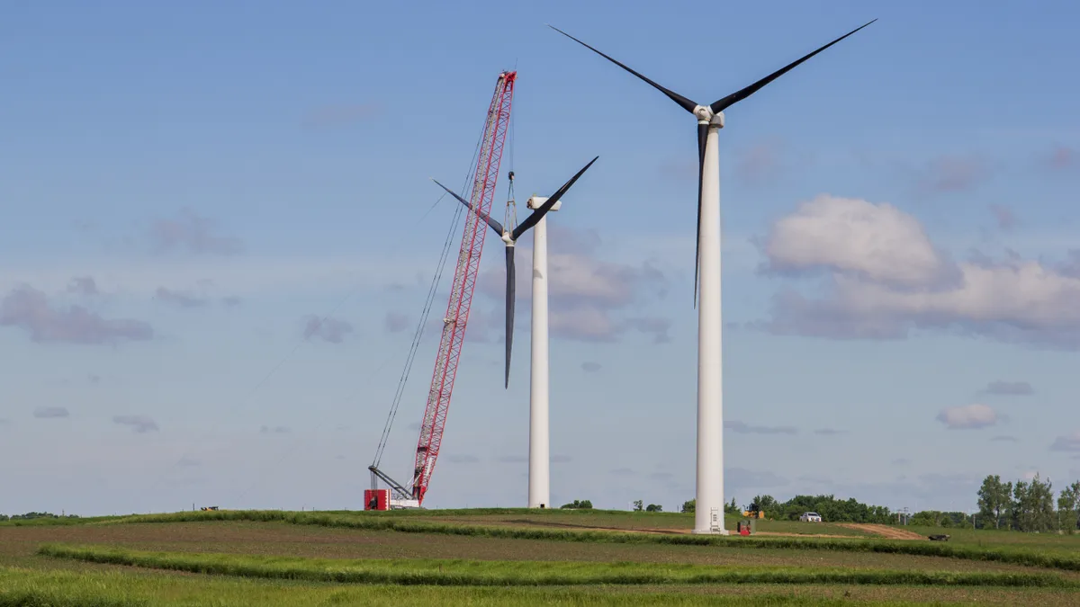 A crane lowers the blades from a wind turbine tower in the middle of a green field.