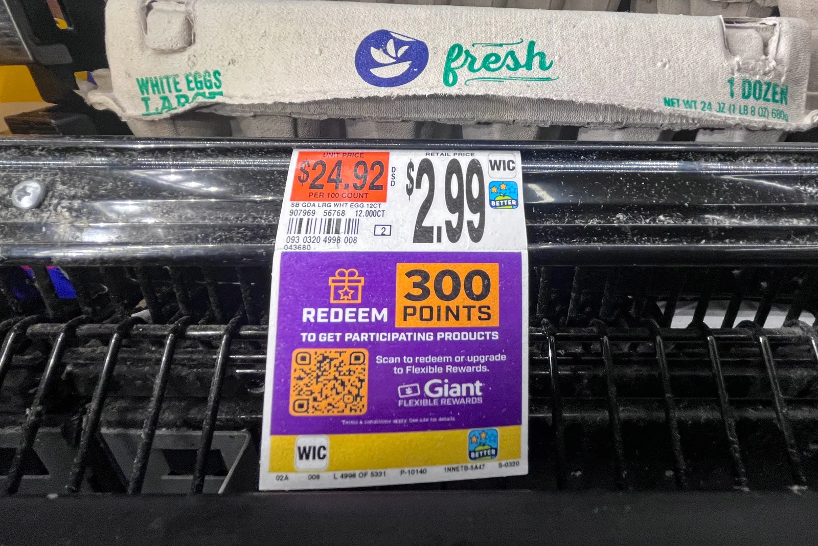 A price tag on a supermarket shelf that reads “$2.99” and “Redeem 300 points” beneath cartons of eggs.