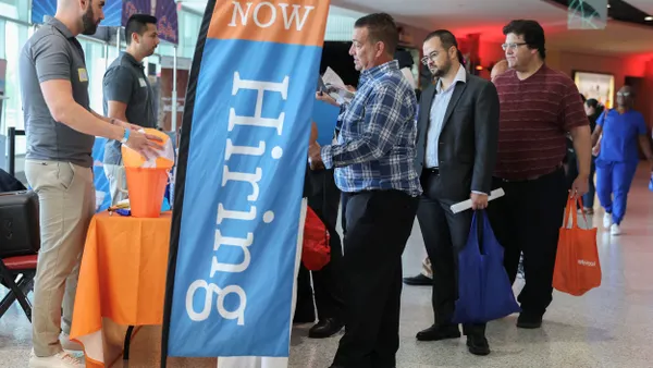 Job seekers line up at a booth to speak with a recruiter at a job fair.