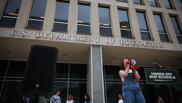 Students rally in front of the U.S. Department of Education, with one speaking into a microphone