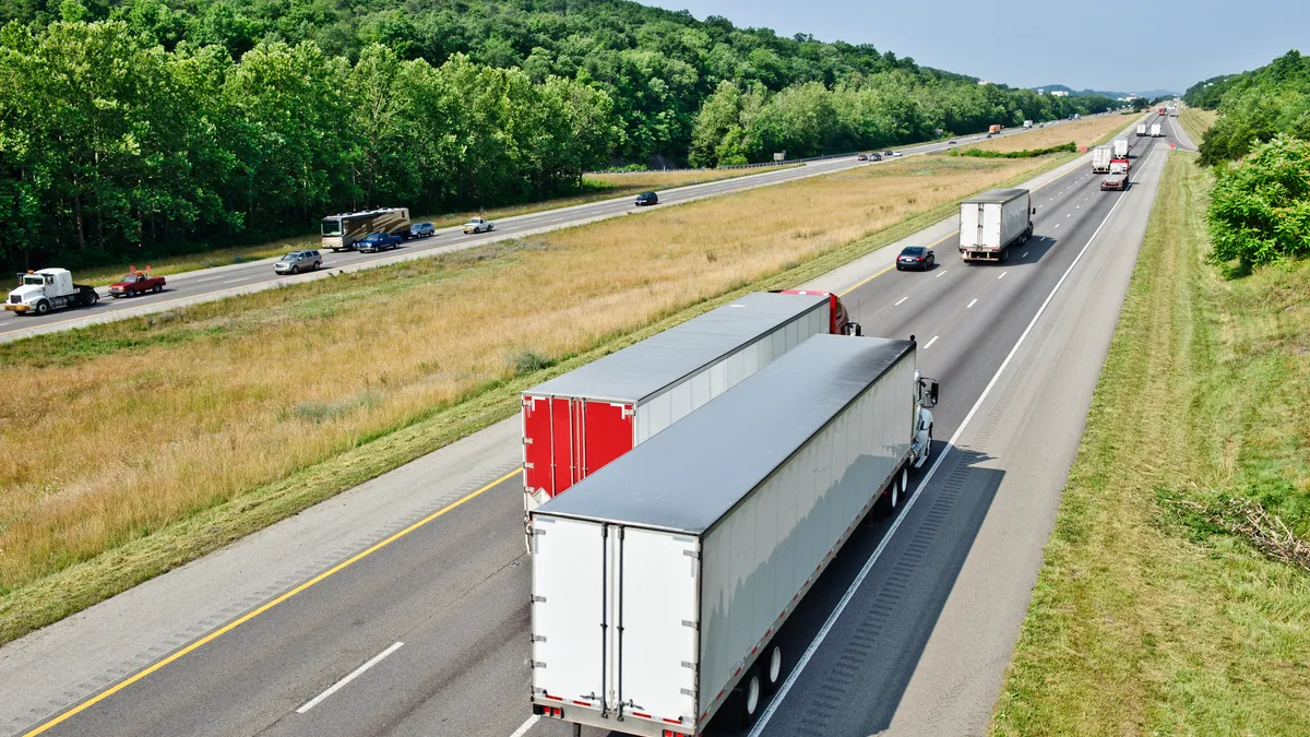 Trucks and vehicles on a divided highway next to a hill of trees.