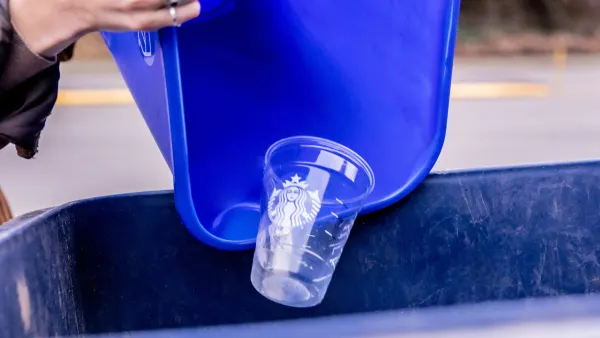 A person tips a blue recycling bin containing a clear plastic Starbucks cup into a larger collection bin.