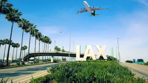 A plane flies low over a sign at LAX.