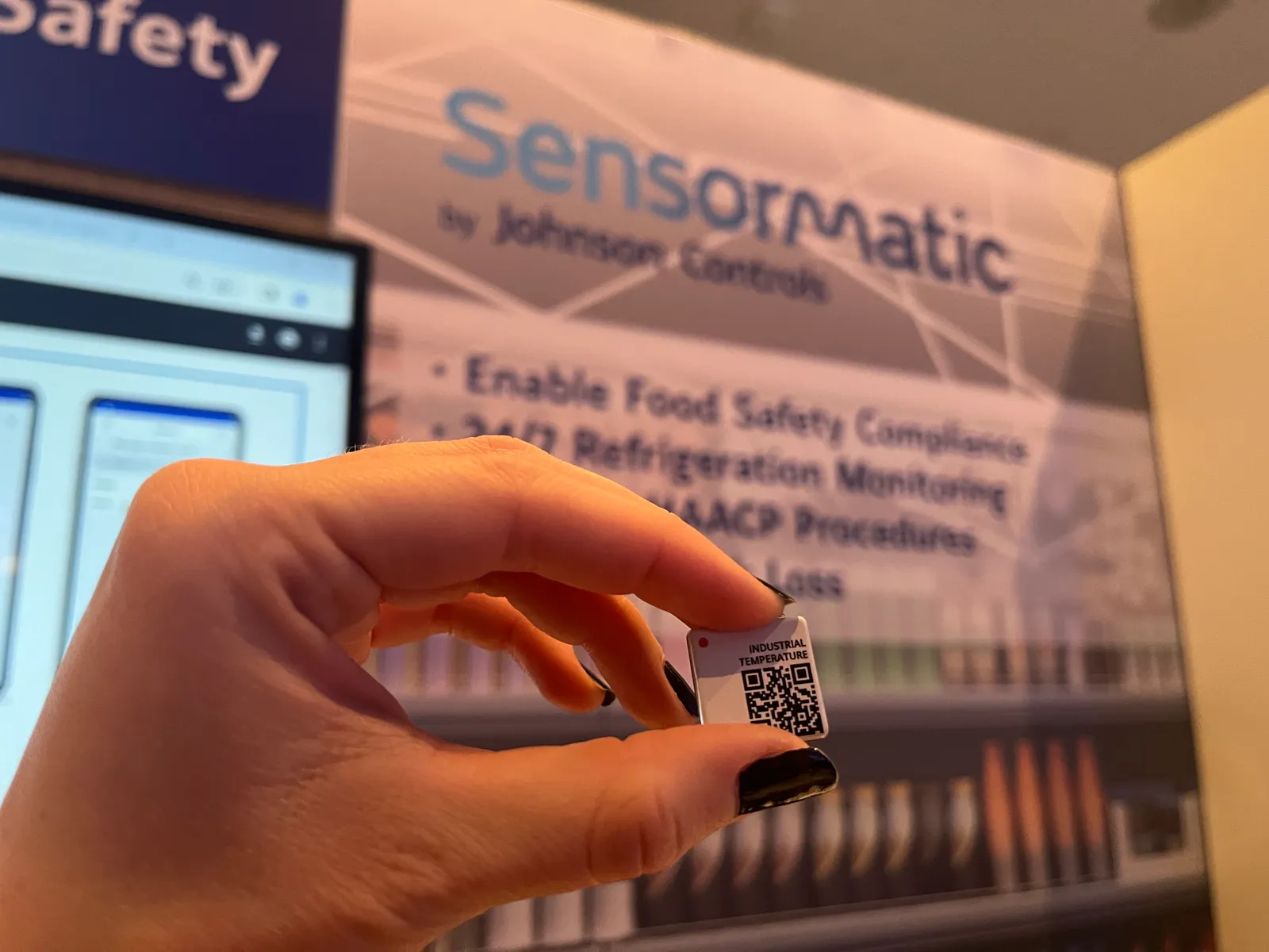 Close-up of a sensor device in front of a Sensormatic sign at a conference booth.