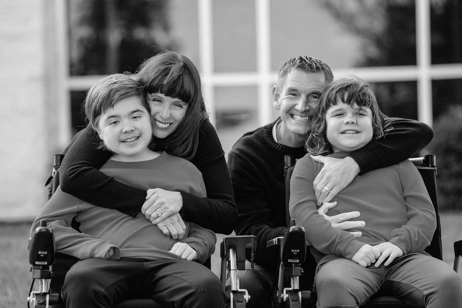 A man and a woman pose for a photograph behind two boys in wheelchairs.
