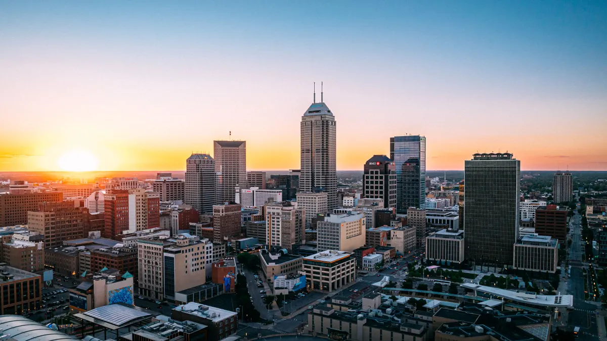 A sunset lowers behind the Indianapolis skyline of tall buildings.