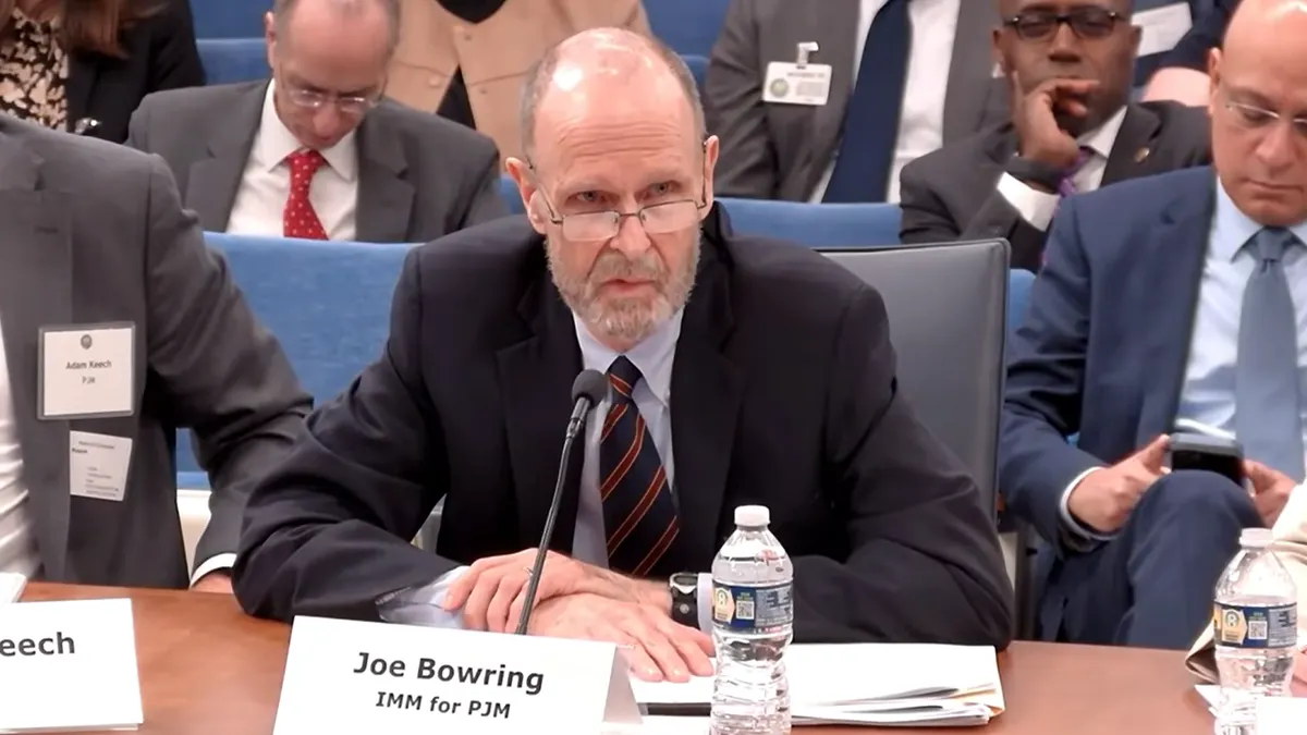 A man in a tie speaks in front of a sign that says "Joe Bowring IMM for PJM."