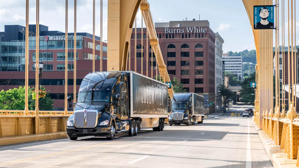 Two Locomation trucks travel across a bridge in Pittsburgh.