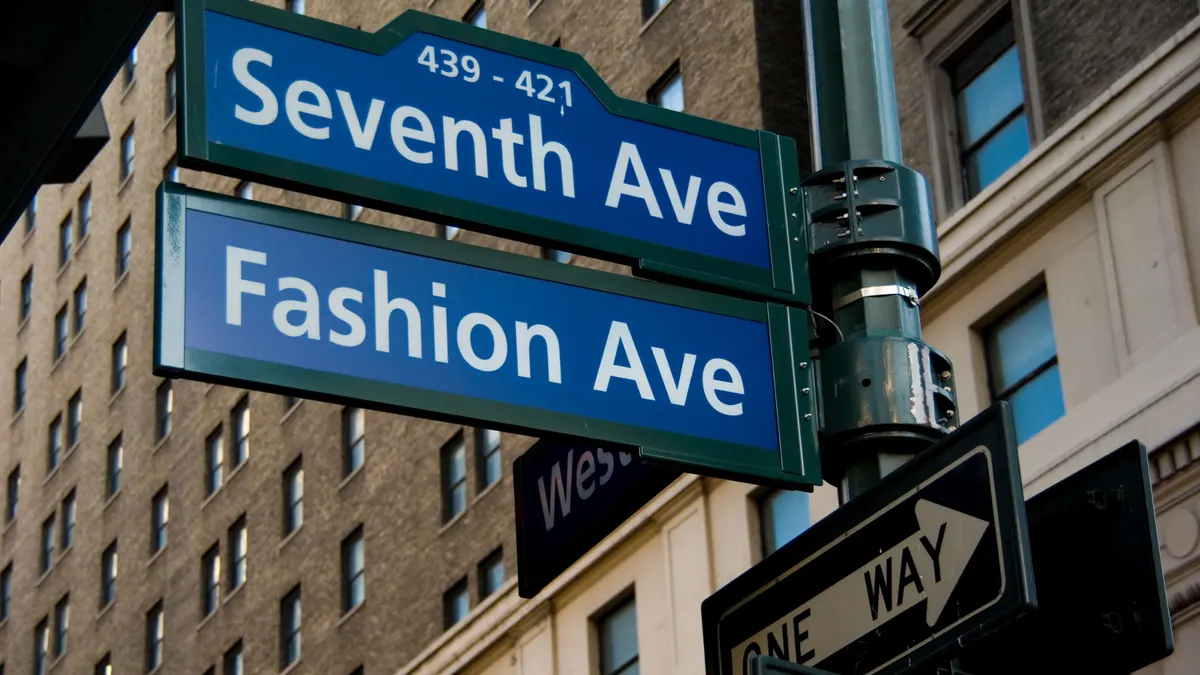 Blue Fashion Avenue street sign above the blue Seventh Avenue street sign in front of a brown brick building.