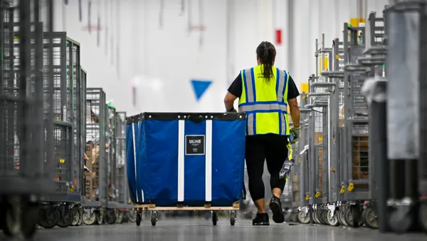 A woman walks with a cart in a warehouse.