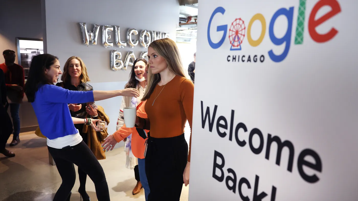 Google employees stand in a hallway greeting each other near a "Welcome back" sign.