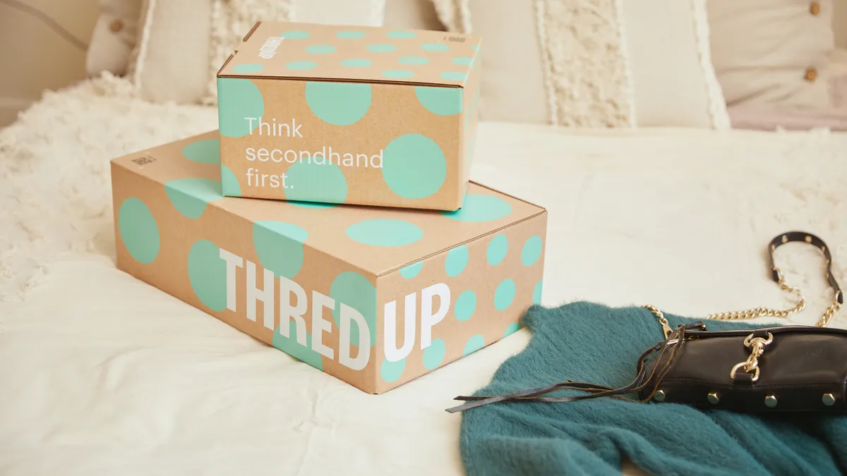 Two ThredUp boxes sitting on top of each other on a bed, with a teal sweater next to them.