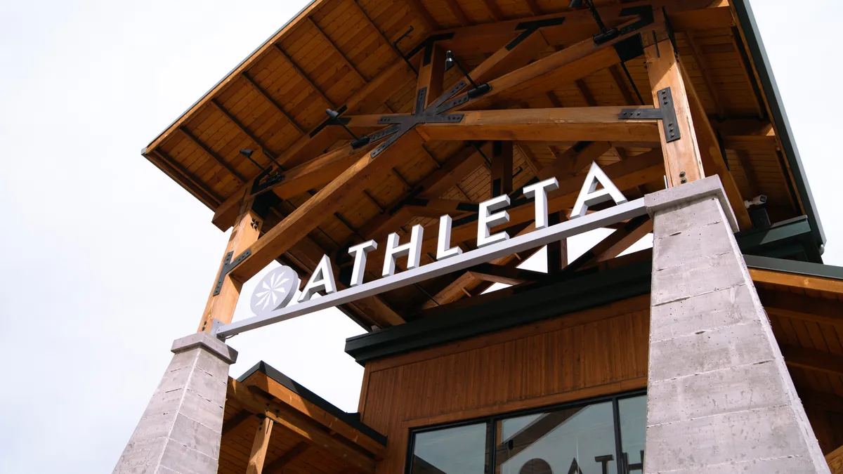 A building with a pitched roof and "Athleta" in big block letters is seen at a slant from below.