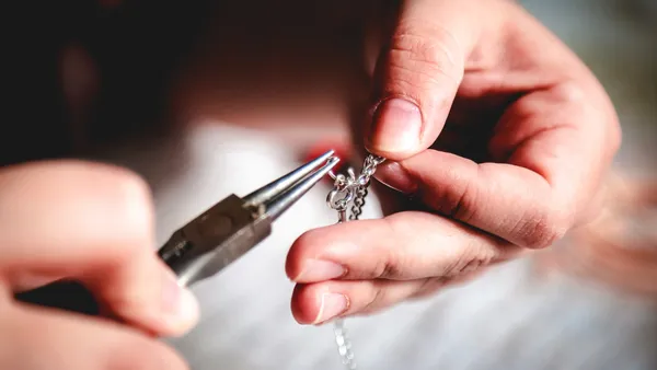 The hands of a young woman are shown crafting a silver jewelry chain.