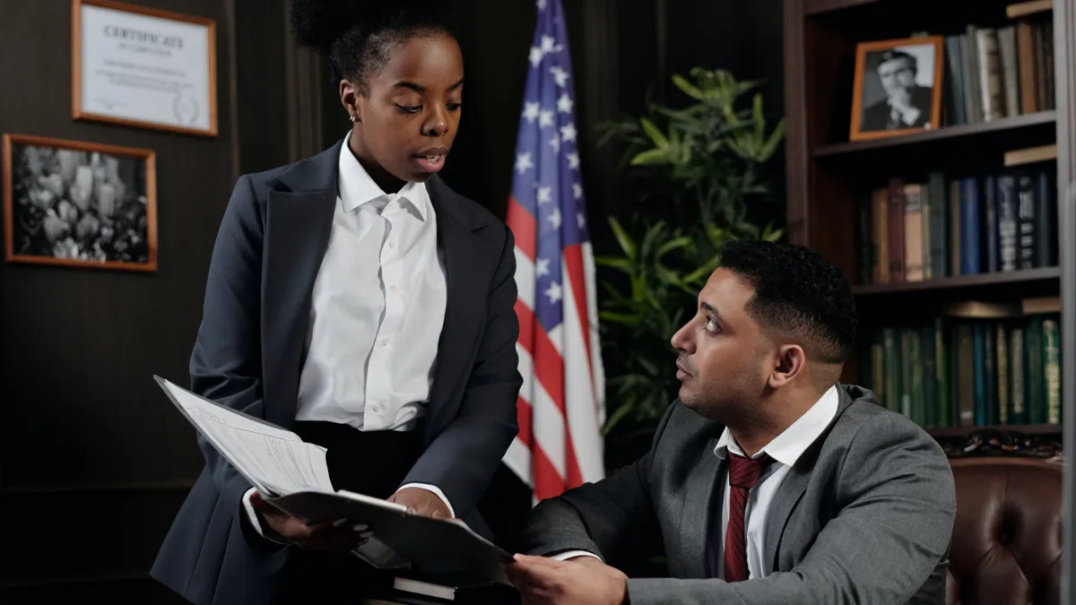 A Black person speaks to a Latinx person in a law office