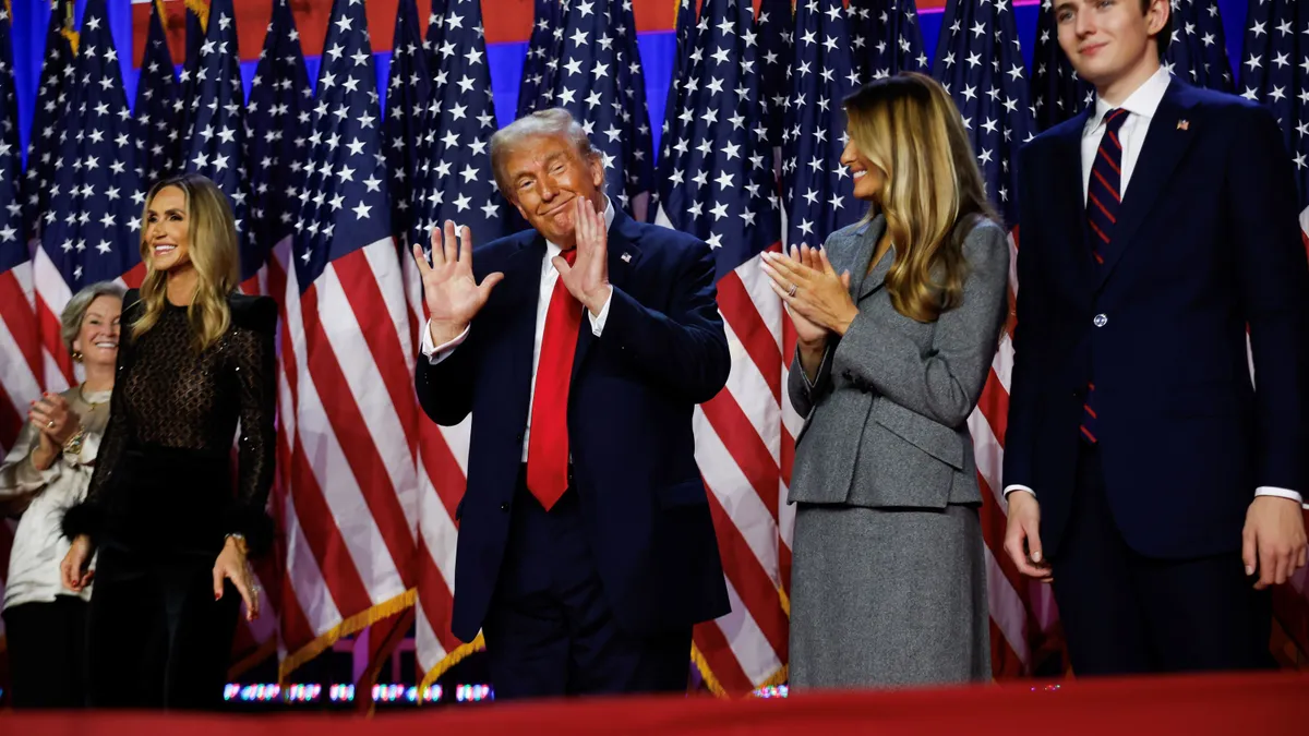 Donald Trump, center, with his hands up, facing the crowd. He's standing next to Melania and son Barron.