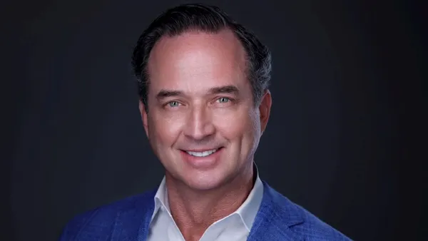 A person wearing a blue jacket and white shirt smiles at the camera.