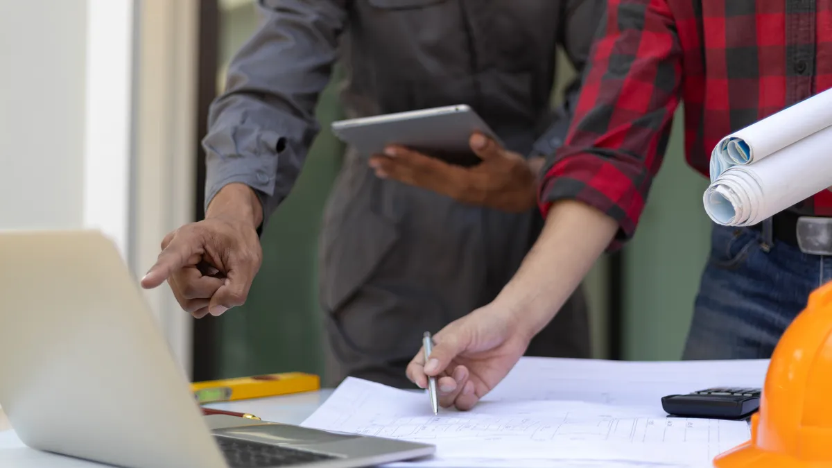 An engineer and business owner look at tables and computers to help with work.